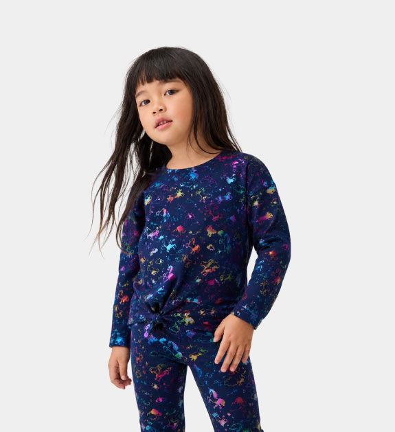 A little girl wearing a galaxy print top and leggings. 