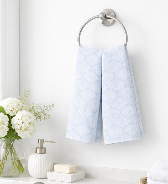 A pair of blue seashell print hand towels displayed in a bathroom. 