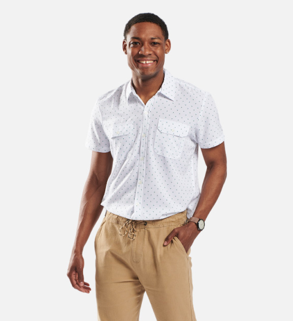 Male model wearing a white with black polka dot collared button-up shirt and beige pants.