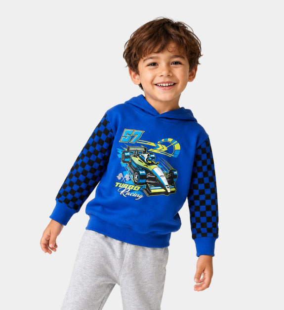 A little boy wearing a blue race car hoody and grey sweatpants. 
