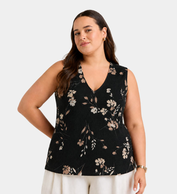 A model wearing a black floral top and cream pants.