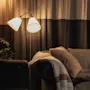 Et hyggeligt opholdsrum med varm belysning fra en gulvlampe, en komfortabel sofa med puder og et tæppe samt bløde gardiner.