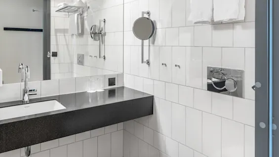 Et moderne badeværelse med hvide flisevægge, mørkt gulv, håndvask med sort bordplade, toilet og friske håndklæder.