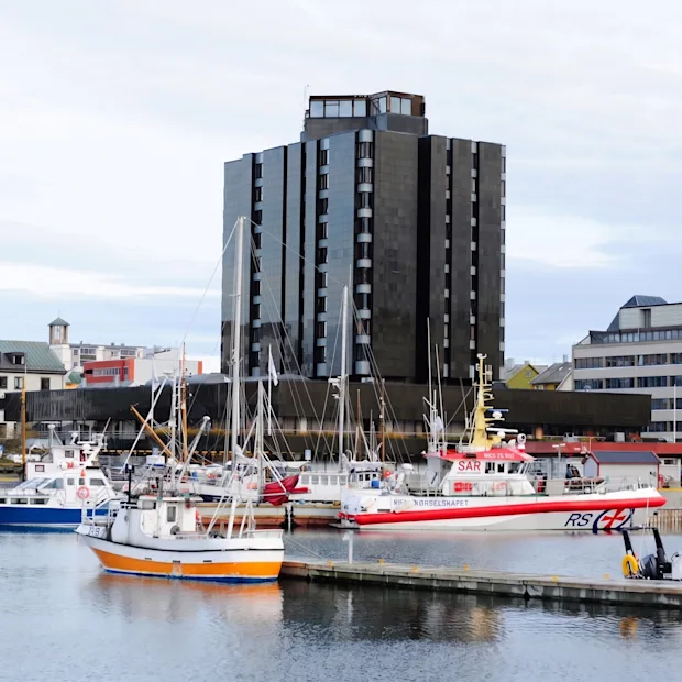 Et mørkt høybygg ved en havn fylt med båter under en overskyet himmel.