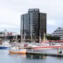 Et mørkt høybygg ved en havn fylt med båter under en overskyet himmel.