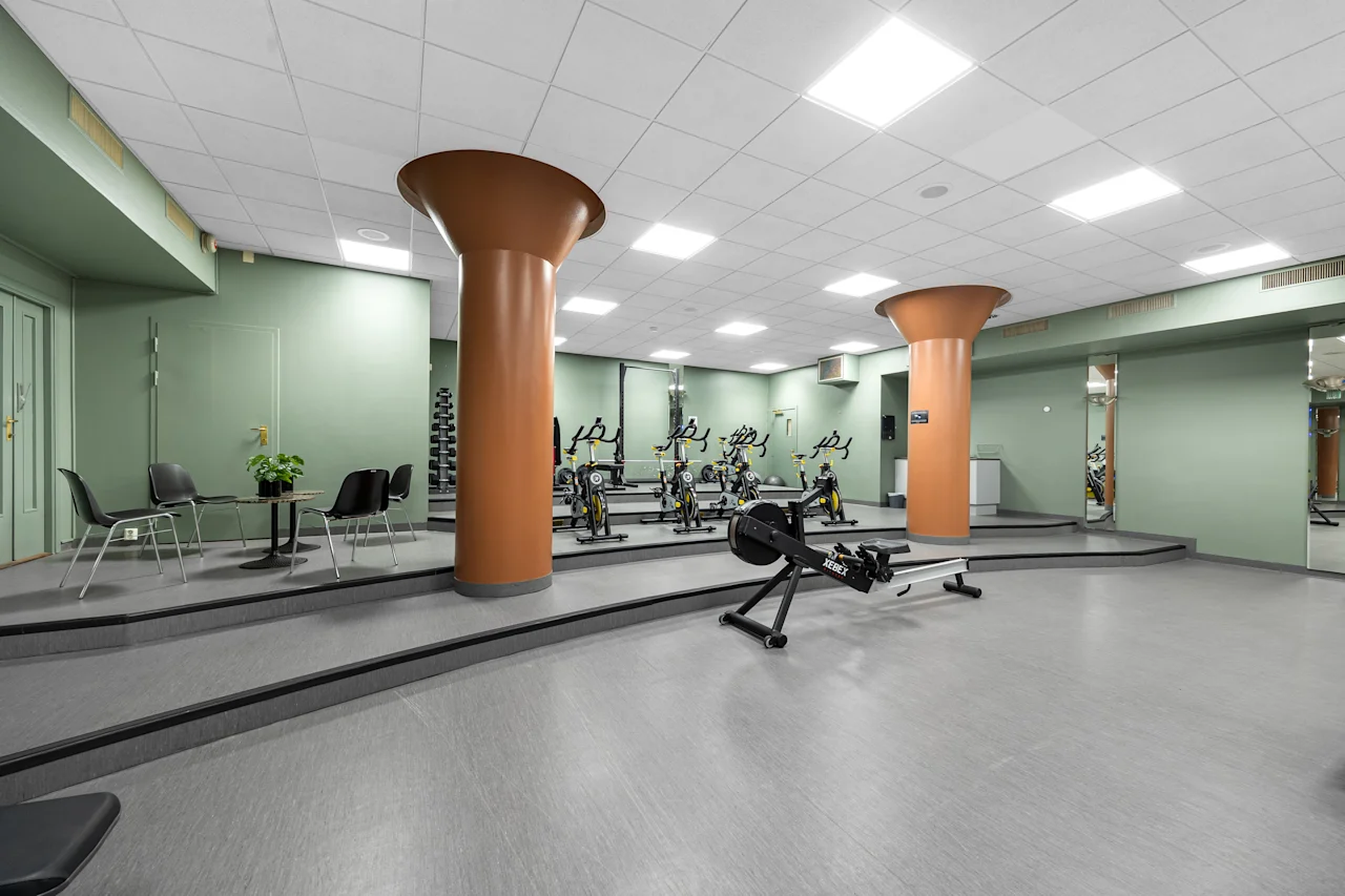 Et romslig hotellgym med treningsapparater, grønne vegger og store oransje søyler.