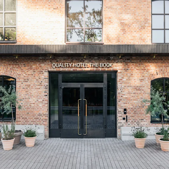 The entrance of a brick hotel building with glass doors and potted plants outside