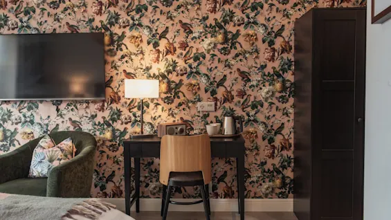 Et hyggeligt hotelværelse på Home Hotel Norre Park i Halmstad med blomstret tapet, et skrivebord, TV og komfortable siddepladser.