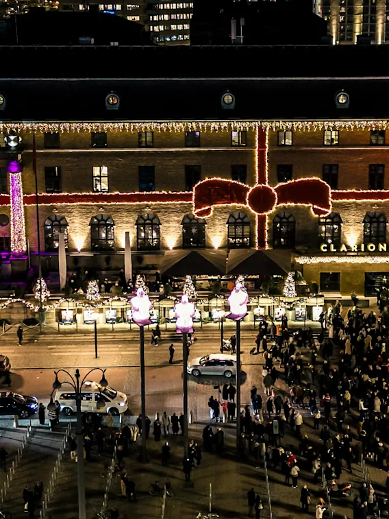 En stor, rikt dekorerad byggnad med neonfärgade lampor och en gigantisk röd rosett vetter mot en livlig gata fylld med en stor folksamling på kvällen.