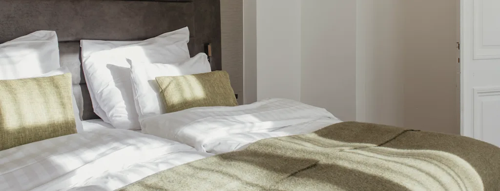 Valoisa ja kutsuva hotellihuone, jossa kaksi sänkyä ja viihtyisä vihreä peitto, johtaa mukavaan oleskelutilaan.