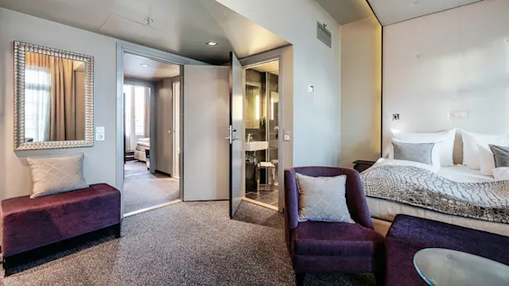 Et moderne hotellrom med luksuriøse møbler, en stor seng, og en åpen dør som fører til et annet rom.