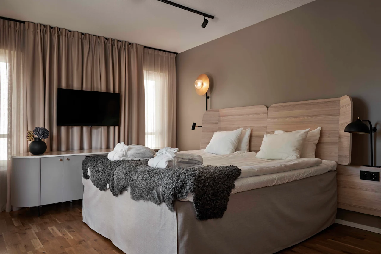 Ett modernt och inbjudande hotellrum med en stor säng, badrockar, en väggmonterad TV och varm belysning.