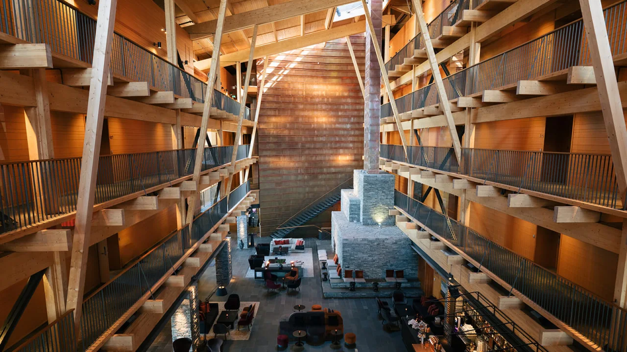 A multi-level wooden interior with crisscrossing staircases and seating areas, illuminated by ample natural light.
