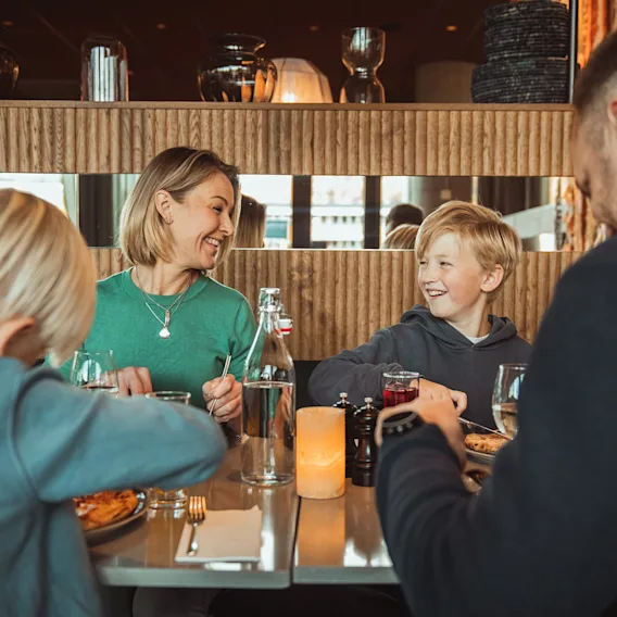 En smilende familie med to unge drenge der nyder en middag sammen ved et moderne restaurantbord.
