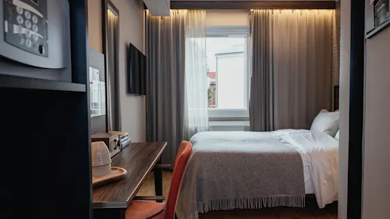 Moderni hotellihuone, jossa on mukava sänky, toimiva työtila ja ikkuna luonnonvalolla.