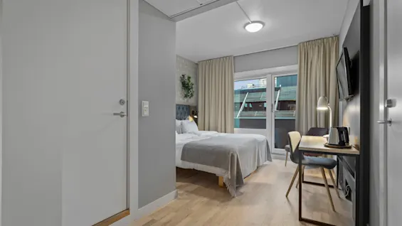 Ett mysigt hotellrum med en säng, en skrivbordsplats och ett stort fönster med utsikt över staden.