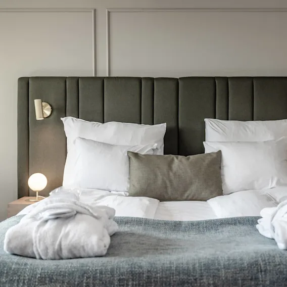 A neatly made bed with white linens and a gray throw, flanked by dimly lit wall lamps in a tranquil bedroom setting.