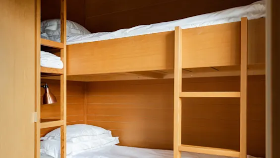 Wooden bunk beds with white bedding, viewed through an open door; a bedroom context.