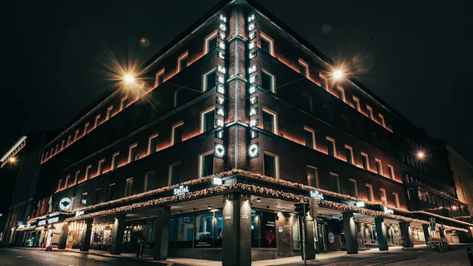 Tiilirakennus yöllä, valaistu katuvaloilla ja koristevaloilla. Kulmassa kyltti HOTEL MESTARI.