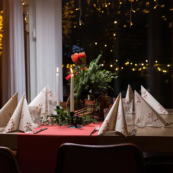 A warmly lit dining table with a floral centerpiece, candles, and neatly folded napkins, against a backdrop of twinkling lights.