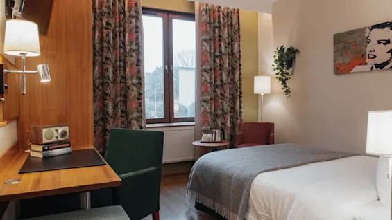 A welcoming hotel room at Home Hotel Kung Oscar with a comfortable bed, a functional desk area, and a cozy seating spot by the window.