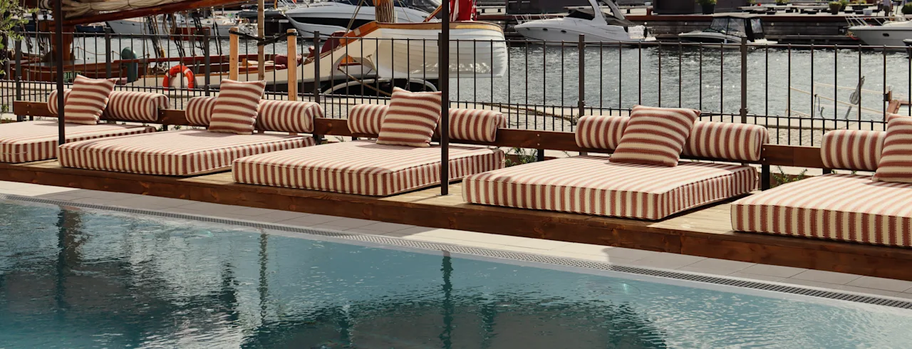 Ett poolområde med solstolar och parasoller med utsikt över en marina med båtar, vilket antyder en avkopplande utomhusmiljö.