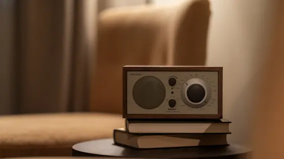 En klassisk radio med teksten 'Audio', 'Bluetooth', 'MODEL ONE' står på bøker på et bord, noe som skaper en koselig og avslappende atmosfære.