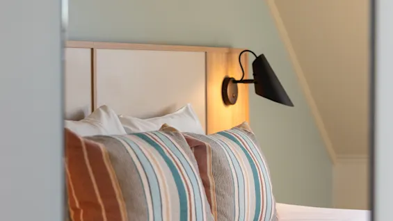 Ett mysigt hotellrum med en säng, randiga kuddar och en varm vägglampa, vilket antyder komfort och avkoppling.
