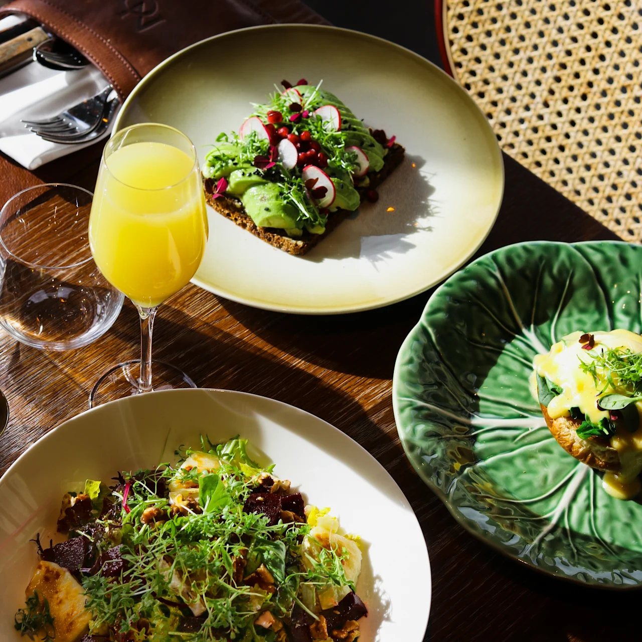 Pöytä katettuna värikkäällä aamiaisella tai brunssilla, avokadoleipää, raikasta salaattia ja eggs benedictiä.