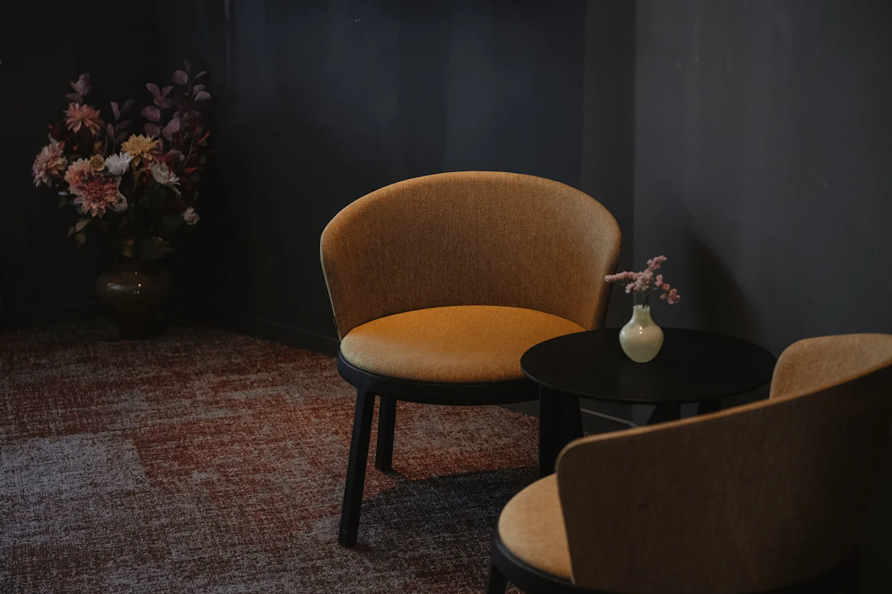 Et koselig sitteområde med to komfortable stoler, et lite bord med en vase og et stort blomsterarrangement.