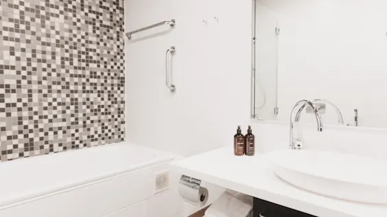 Et rent, moderne hotelbadeværelse med et hvidt badekar, mosaikflisevæg og en elegant vask med toiletartikler og friske håndklæder.