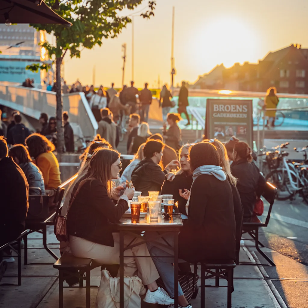 People enjoying food and drinks outdoors at sunset. Broens Gadekokken, Broens Street Food, a food market in Copenhagen.