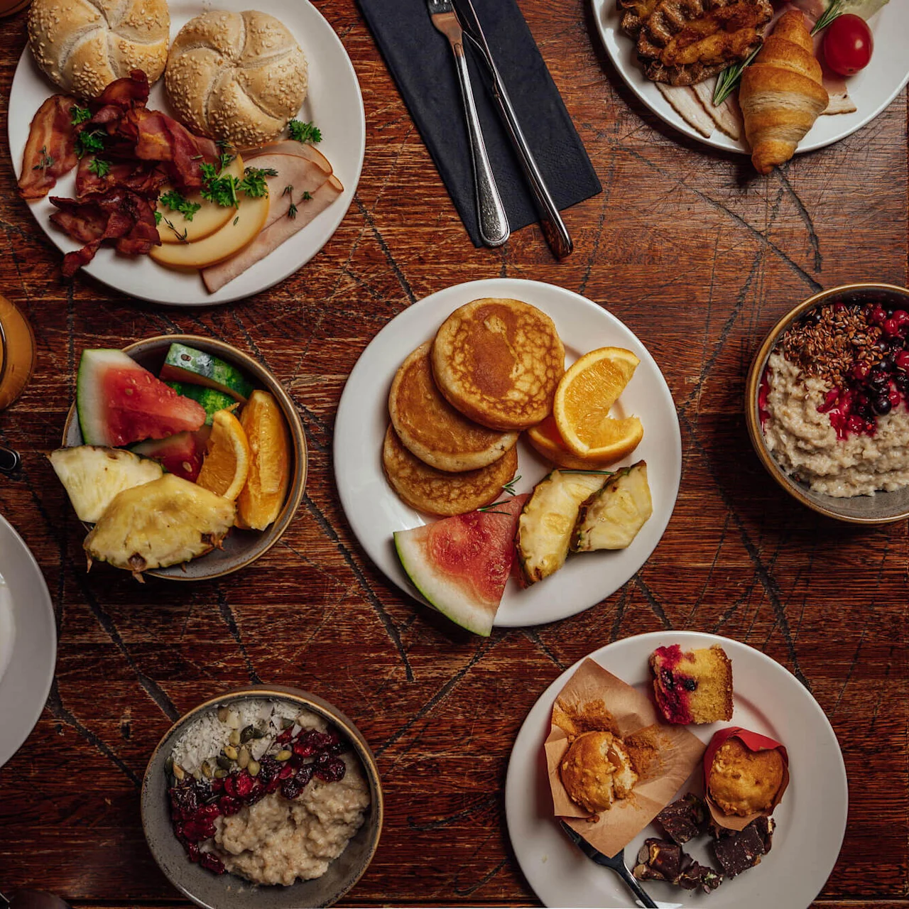 A variety of breakfast items spread on a wooden table, suggesting a communal meal.