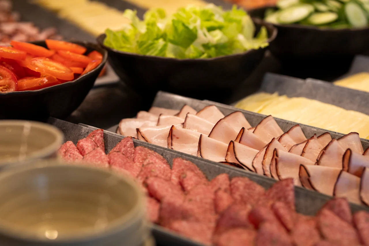 En livlig buffé med färska skivade tomater, krispig sallad, diverse kallskuret och ost, redo för gästerna att njuta av.