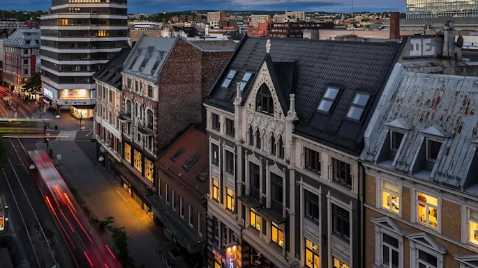 Historic buildings line a street at twilight; a blurred vehicle leaves light trails; urban environment.
