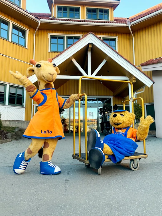 Maskottene Lollo giraff og bjørnen Bernie på en bagasjevogn utenfor hotellinngangen.