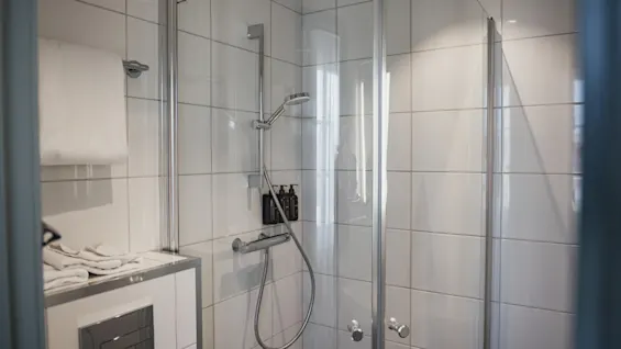 Ett rent och modernt badrum med en kaklad duschkabin med glasdörr, duschhuvud och toalettartiklar.