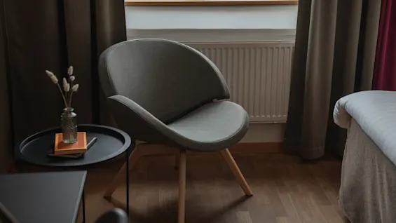 A comfortable grey armchair next to a small table with a vase and books, in a room at Home Hotel Uppsala.