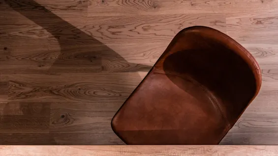 A brown leather chair is partially visible on a wooden floor, casting a shadow under warm lighting.