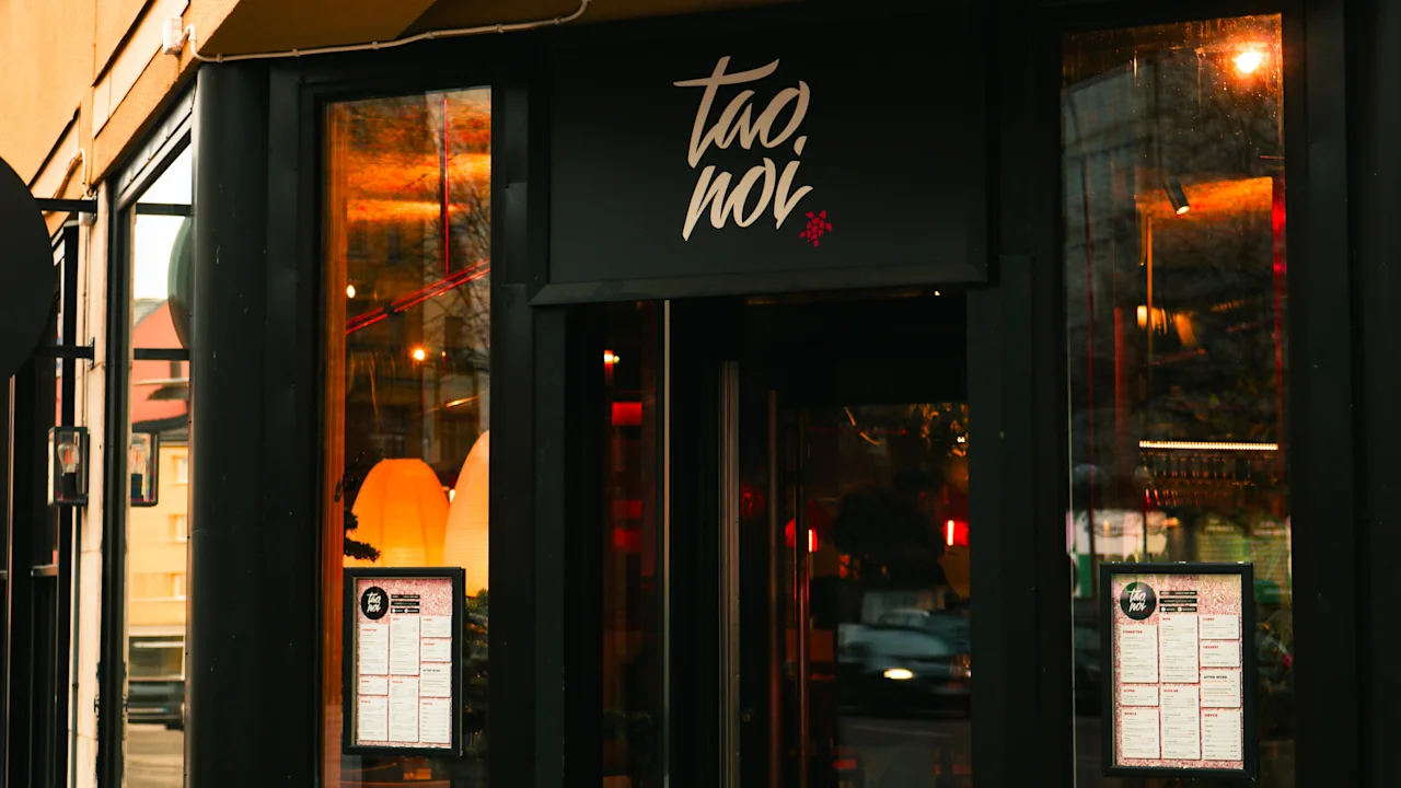 En restaurantindgang med et skilt, der læser tao noi. Menuer vises i vinduerne, og varme lys gløder indenfor.