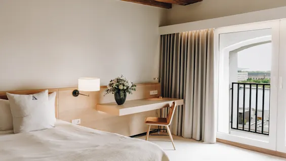 Ljust hotellrum med säng, skrivbord i trä och en balkong med utsikt över vattnet