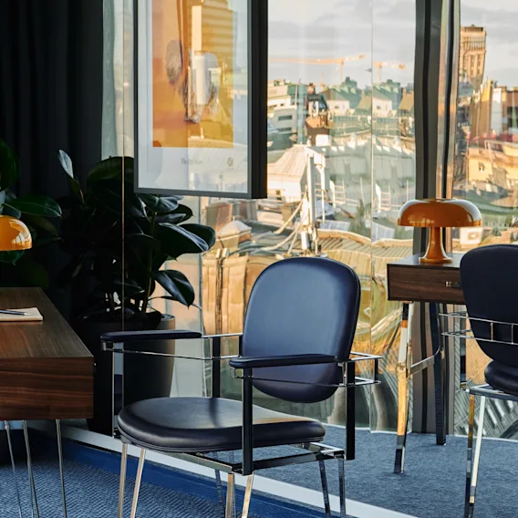 En ljus, modern arbetsplats med utsikt över stadens silhuett, med stilrena skrivbord och stolar. Stratum Suite på Clarion Hotel Sign i Stockholm.