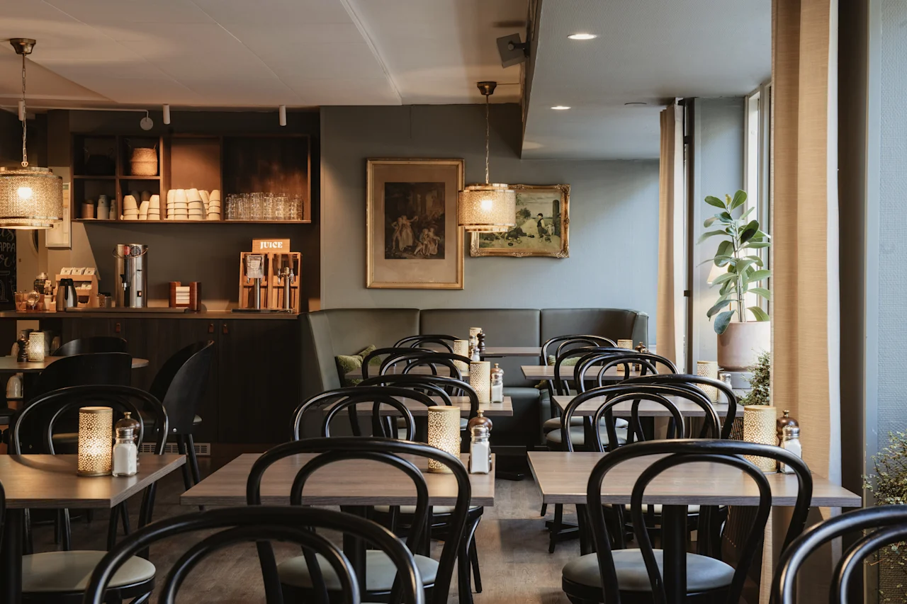 En mysig restauranginteriör med tomma bord och stolar, redo för gäster. En självbetjäningsdisk med JUICE är synlig.