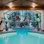 Ett inbjudande inomhuspoolområde med bubbelpool, omgivet av frodiga gröna växter och stora fönster, under ett varmt trätak.