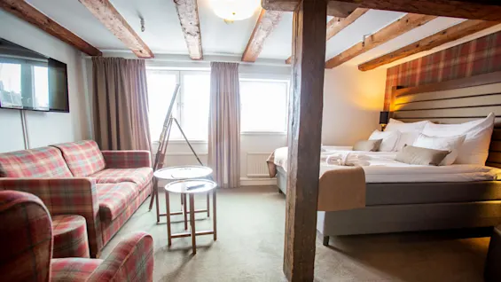 A cozy hotel room with a plaid sofa, exposed wood beams, and a neatly made bed, creating a warm, inviting atmosphere.
