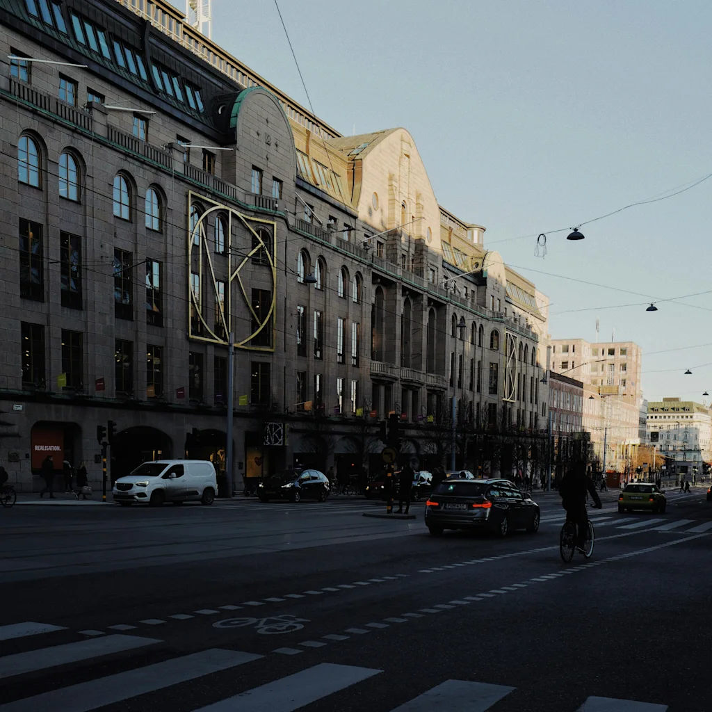 Kaupunkikatu, jossa on historiallisia rakennuksia, autoja ja pyöräilijä aurinkoisena päivänä.