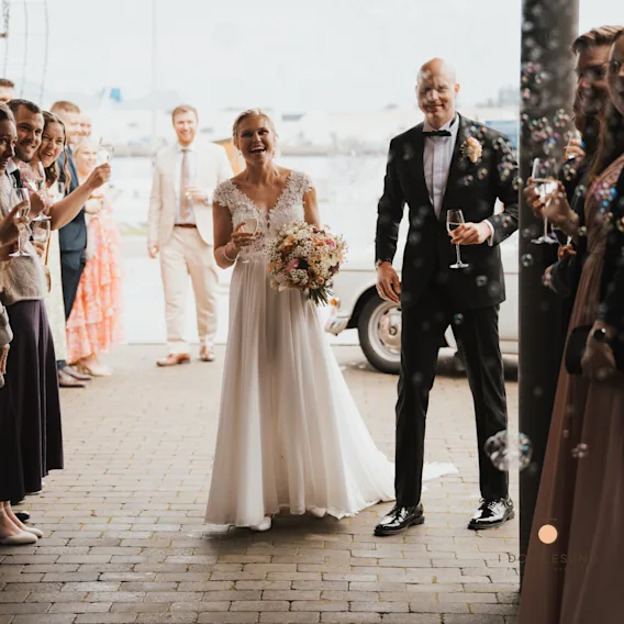 Nygift par med champagneglass går gjennom gjester som blåser såpebobler utendørs.