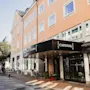 Hotellin sisäänkäynti aurinkoisella kadulla, jossa on musta markiisi, jossa lukee HOTEL CARDINAL. Polkupyöriä on pysäköity lähelle.