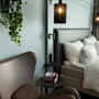 Et koselig hotellrom med seng, hvit sengetøy, komfortabel lenestol og hengende plante, opplyst av stilige vegglamper.