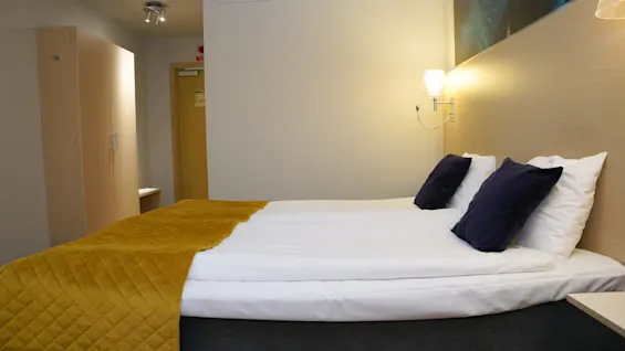 Viihtyisä ja moderni hotellihuone Quality Hotel Sundsvallissa mukavalla sängyllä, valkoisilla liinavaatteilla ja lämpimällä keltaisella peitolla.